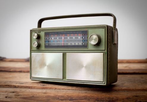 Close up slightly desaturated color photo of a vintage green portable radio sitting on a wood table.